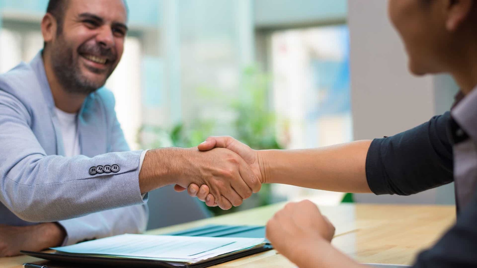 Corretora de seguros cumprimentando cliente sobre apólice em escritório claro